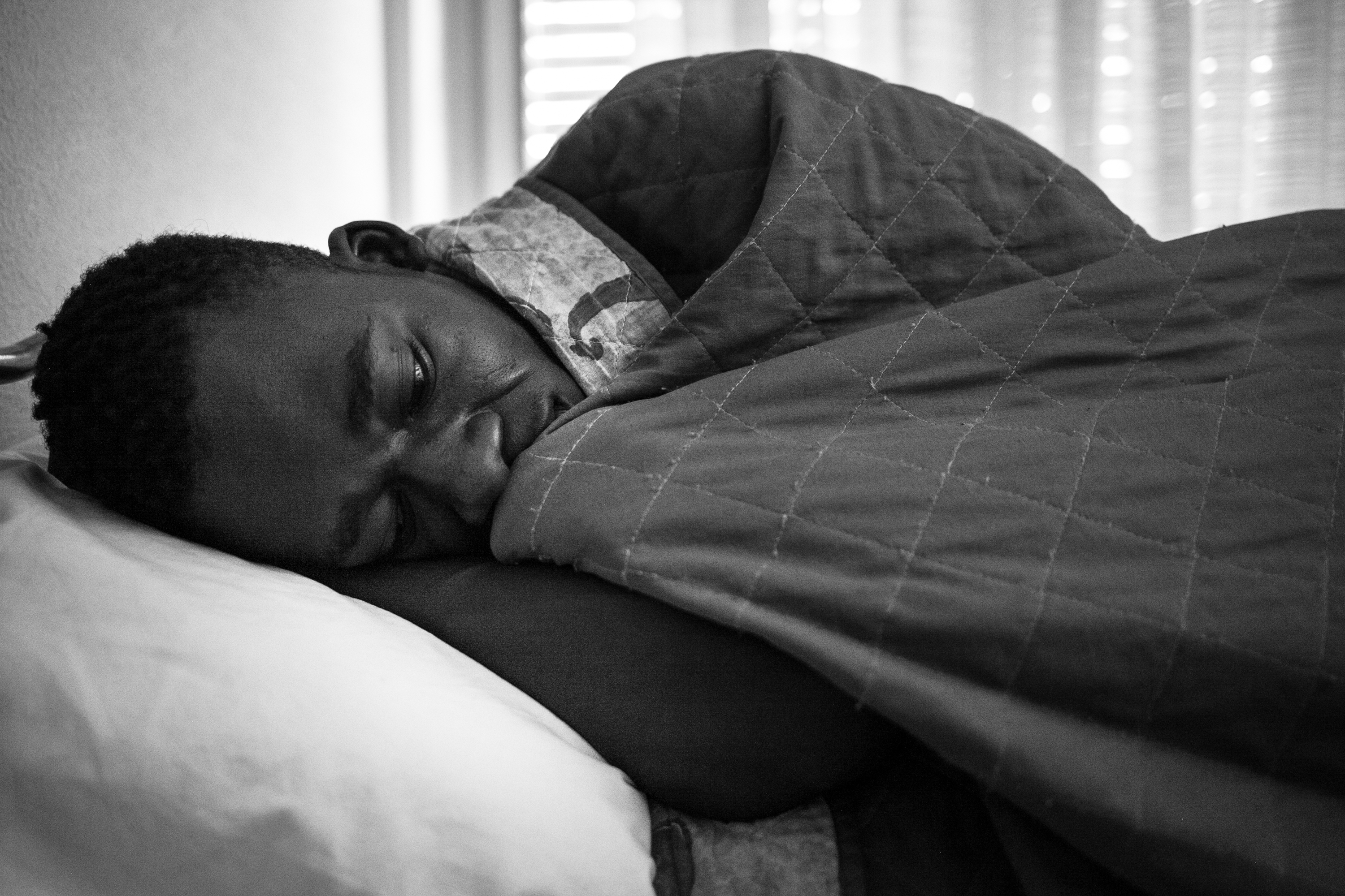 Malick lies on his bed in Hotel Colibri, in the city of Biella, where he lives since August 2016. He shares room with three more people from Gambia and Senegal. (Photo: César Dezfuli)